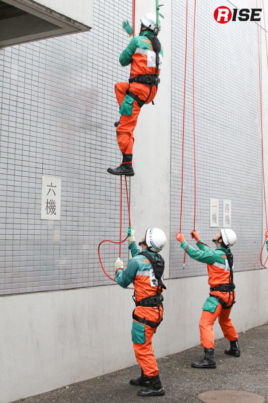 登はん員が懸垂ロープを掴むと、補助員がロープを足に巻き付ける。